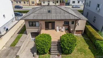 Luftaufnahme des Hauses mit einer gepflasterten Terrasse, Außentreppe und gepflegten Büschen im Vorgarten.
