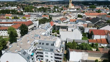 Luftaufnahme der Stadt mit Wohngebäuden und einem Kirchturm im Hintergrund unter blauem Himmel.