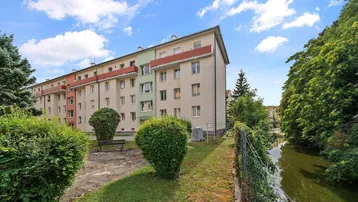 Mehrfamilienhaus mit Balkonen und gepflegten Grünflächen am Wasserlauf.