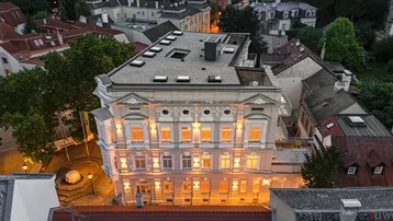 Luftaufnahme des beleuchteten Gebäudes bei Dämmerung, umgeben von städtischer Architektur.