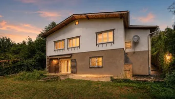 Hausfassade bei Sonnenuntergang mit Garten und umliegender Natur.