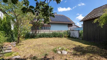 Gartenbereich mit Blick auf das Nachbarhaus mit Solaranlage und blühenden Bäumen.