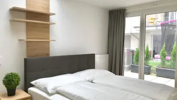 Helles Schlafzimmer mit Holzelementen, großem Fenster und Zugang zu einem Außenbereich.