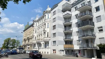 Blick auf eine belebte Stadtstraße mit Gebäuden unterschiedlicher Architekturstile und Balkonen.