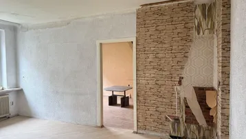 Unfertiges Wohnzimmer mit Kaminanschluss, Holzboden und Renovierungsbedarf.