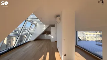 Helles Dachgeschoss-Wohnzimmer mit großen Schrägfenstern, Holzboden und Blick über die Stadt.