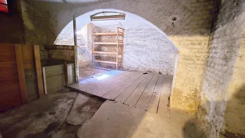 Alter Kellerraum mit Gewölbedecken und unebenen Wänden, teilweise mit Holzboden und einem Regal.
