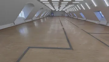 Großer, heller Raum mit schrägen Wänden, vielen Fenstern und Reihen von Deckenleuchten.