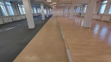Großes, offenes Büro mit Säulen, einer Mischung aus Teppich- und Holzböden sowie vielen Fenstern.