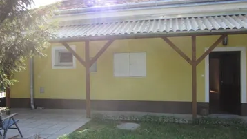 Überdachte Terrasse mit gepflastertem Bereich und angrenzender Rasenfläche am Haus.