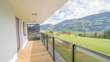 Geräumiger Balkon mit Holzboden und Glasgeländer bietet einen weiten Blick auf die grüne Berglandschaft.