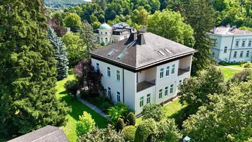 Luftaufnahme einer eleganten Villa mit Satteldach, umgeben von üppigem Grün und hohen Bäumen.