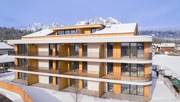 Modernes Apartmentgebäude mit Holzfassade und Balkonen vor verschneiter Bergkulisse.
