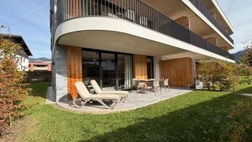 Moderne Wohnanlage mit großzügiger Terrasse, Liegestühlen und einem gepflegten Rasenbereich im Freien.