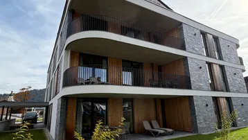 Modernes Mehrfamilienhaus mit geschwungenen Balkonen und Steinverkleidung in alpiner Umgebung.
