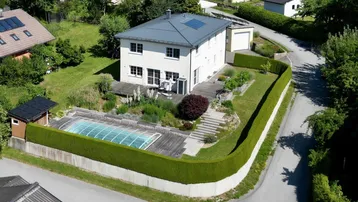 Luftaufnahme eines Einfamilienhauses mit Pool, Garten und gepflegter Hecke in ländlicher Umgebung.