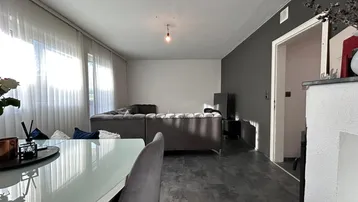 Heller Wohn- und Essbereich mit modernem Sofa, dunklem Boden und großen Fenstern.