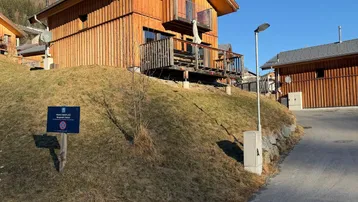 Modernes Holzhaus in alpiner Umgebung mit sonnigem Hanggrundstück und klarem Himmel.