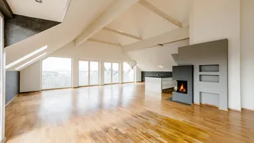 Helles, offenes Dachgeschoss mit Holzboden, Kamin und Zugang zu mehreren Balkonen.