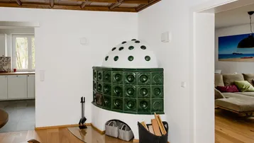 Traditioneller Kachelofen in einem Wohnbereich mit Holzboden und Kassettendecke, verbindet Ess- und Wohnzimmer.
