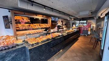 Geräumiger Bäckereiverkaufsraum mit langen Theken, vielen Backwaren und Holzparkettboden im Fischgrätmuster.