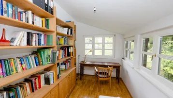 Helles Arbeitszimmer mit Holzboden, Bücherregalen und einem Schreibtisch am Fenster.