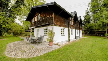 Traditionelles Haus mit Holzfassade und weißem Putz, umgeben von einem grünen Garten mit Terrasse.