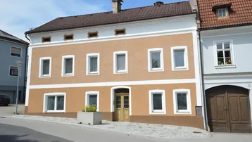 Vorderansicht eines traditionellen Gebäudes mit ockerfarbener Fassade und weißen Fensterrahmen an einer Straße.