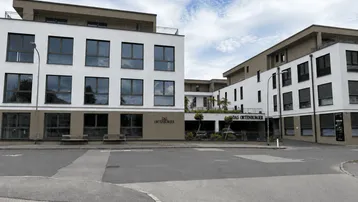 Moderne Wohnanlage mit weißer und brauner Fassade, großen Fenstern und einem Straßenzugang unter blauem Himmel.