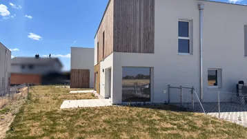 Moderne Neubauten mit Holzfassadenelementen und großen Fenstern, umgeben von einer noch ungestalteten Gartenfläche.