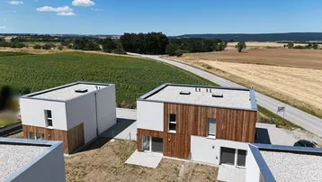 Moderne Reihenhäuser mit Flachdächern und Holzfassaden, umgeben von Feldern und einer Landstraße.