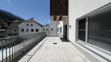 Lange, sonnige Terrasse mit Fliesenboden, Metallgeländer und Bergblick.