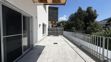 Geräumige, geflieste Terrasse mit Metallgeländer und Blick ins Grüne.