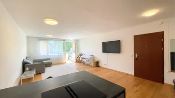Heller offener Wohnbereich mit moderner Kücheninsel, Holzboden und Zugang zum Balkon.