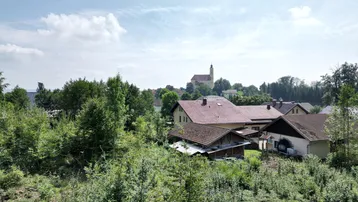 Ländliche Ansicht eines Dorfes mit Kirche im Hintergrund, umgeben von viel Grün und Bäumen.