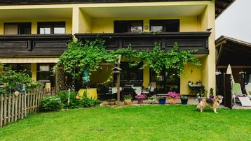 Großzügiger Gartenbereich vor dem Haus mit Rasenfläche, Terrasse und Balkon, umgeben von Natur.