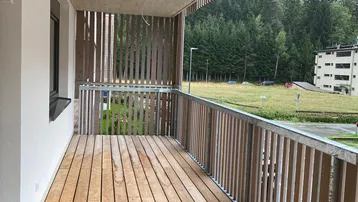 Geräumiger Balkon mit Holzboden und Blick ins Grüne, umgeben von einer modernen Holzlamellenbrüstung.