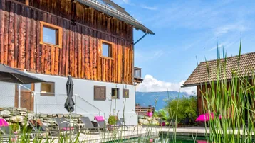 Natürlicher Schwimmteich mit Liegestühlen und einem traditionellen Holzhaus im Hintergrund.