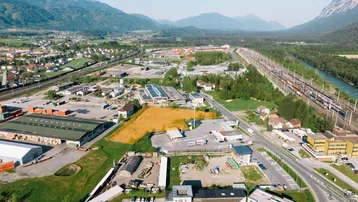 Luftaufnahme eines Grundstücks in einer Industriezone mit Bergen im Hintergrund und Fluss.