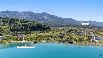 Luftaufnahme des Faaker Sees mit umliegender Landschaft und Bergen, die Lage der Immobilie markierend.