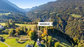 Luftaufnahme eines Hauses in einem malerischen Tal, umgeben von grünen Wäldern und Bergen.