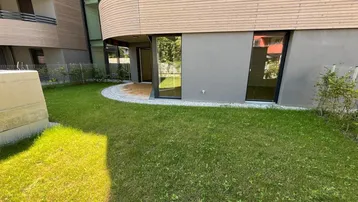Außenbereich eines modernen Gebäudes mit Rasenfläche und einer kleinen gepflasterten Terrasse.