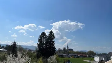 Blick auf eine ländliche Umgebung mit Dorf, Bergen und blühenden Bäumen unter blauem Himmel.
