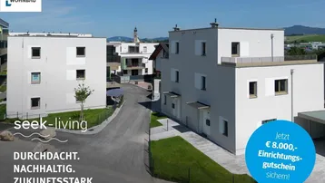 Moderne Neubauten in einer Wohnsiedlung mit Flachdächern, Grünflächen und Bergblick.