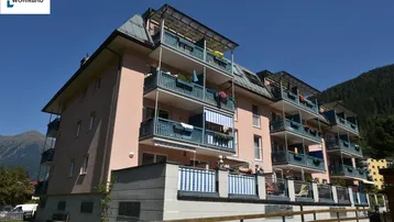 Modernes Mehrfamilienhaus mit Balkonen und Bergblick unter blauem Himmel.