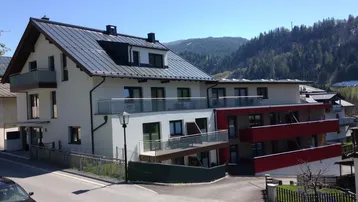 Modernes Wohngebäude mit mehreren Balkonen und Bergblick in sonniger Umgebung.