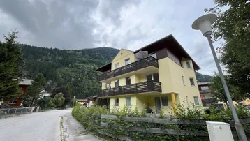 Mehrstöckiges Gebäude mit Balkonen und alpiner Umgebung unter bewölktem Himmel.