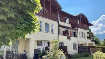 Außenansicht eines Mehrfamilienhauses mit Balkonen, Terrassen und gepflegtem Gartenbereich unter blauem Himmel.