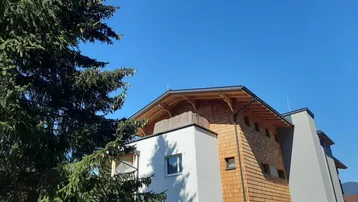 Modernes Gebäude mit Holzfassade und markantem Dachüberstand unter blauem Himmel.