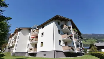 Mehrstöckiges Wohngebäude mit Balkonen und grüner Umgebung unter blauem Himmel.